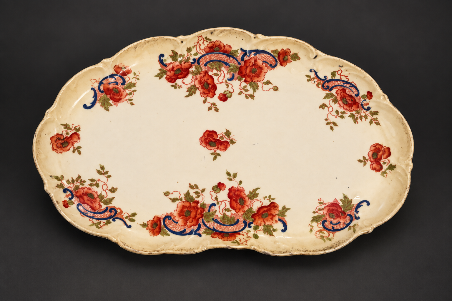 Illustrative studio view of the cream scalloped platter with red flowers and blue ornament