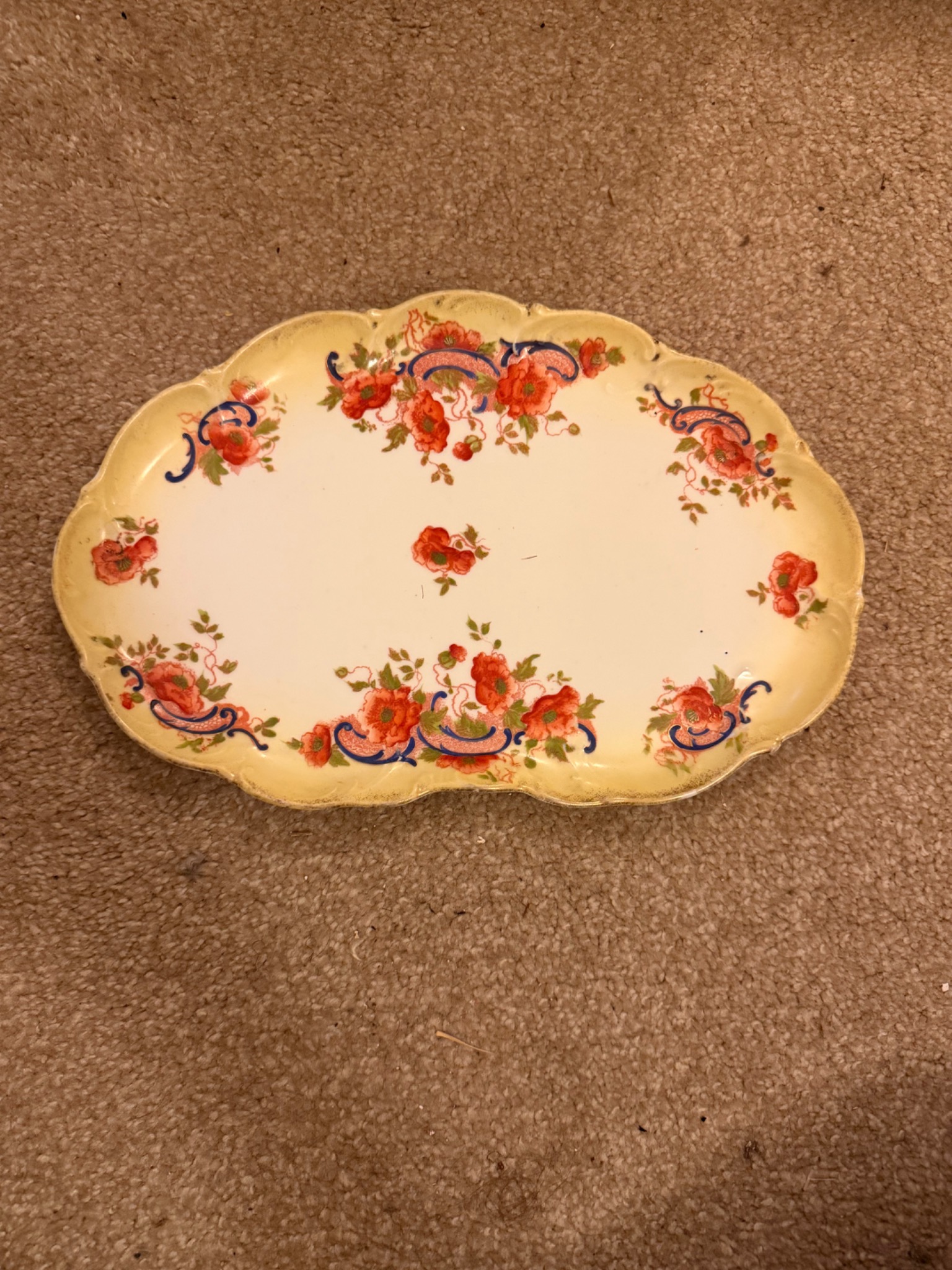 Original unedited photograph of the floral ceramic platter on a carpet, showing its scalloped rim and visible wear